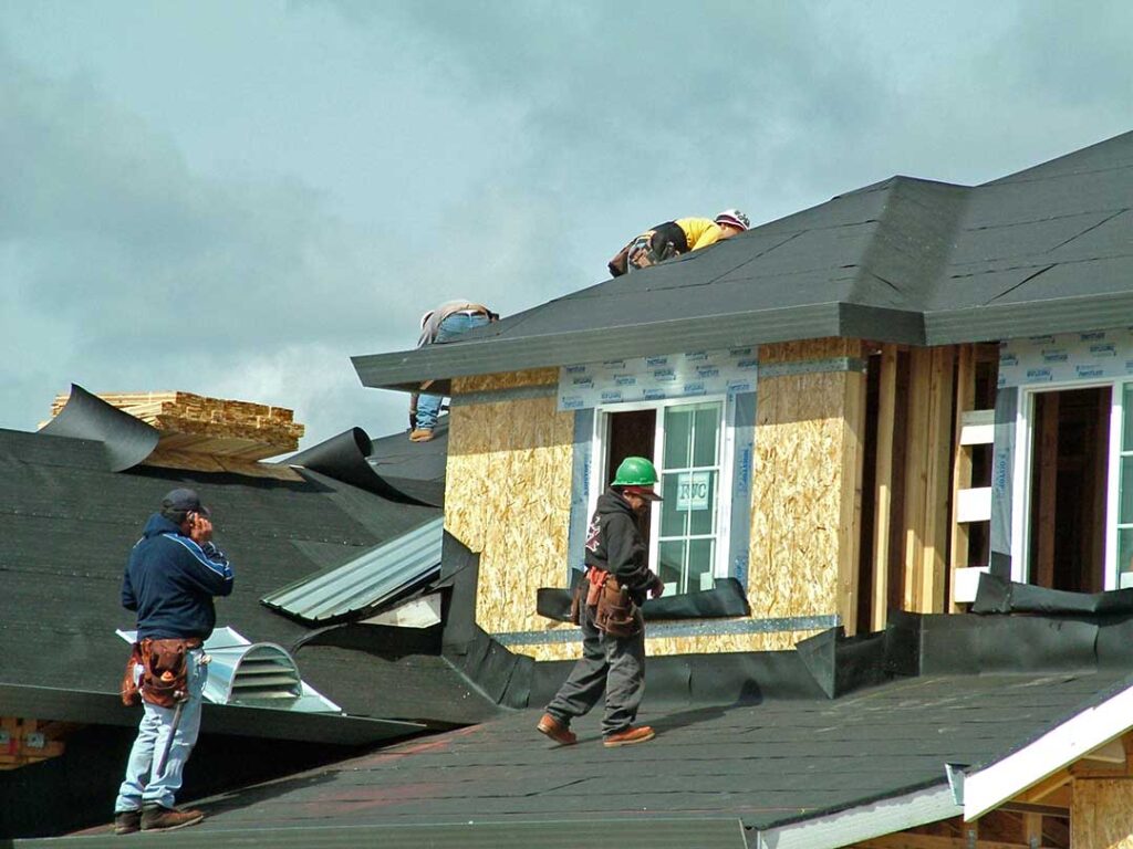 Metal, slate, tile, and asphalt roofing samples arranged beside a snow-dusted residential roof.